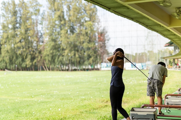 Aziatische vrouw die zijn golfschommeling uitoefent bij de golf driving range.