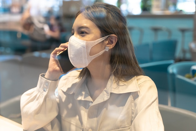 Aziatische vrouw draagt maskers die op slimme telefoon praten tijdens het reizen op de luchthaventerminal