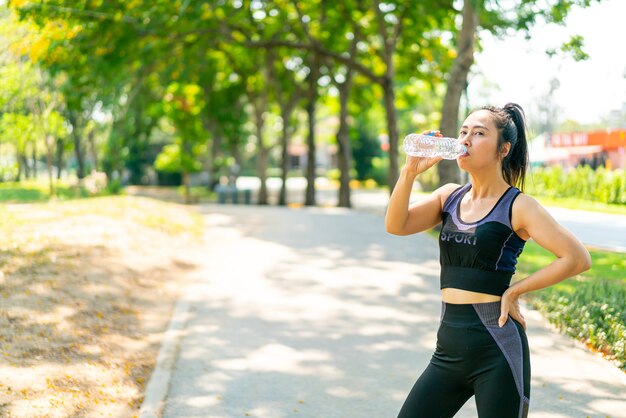 Aziatische vrouw drinkwater in sportwear na het sporten in het park