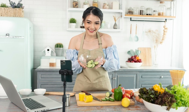 Aziatische vrouw food blogger kookt salade voor de camera van de smartphone tijdens het opnemen van vlog-video