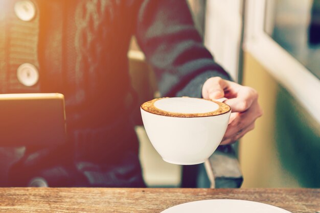 Aziatische vrouw hand houden van koffie en het gebruik van tablet in koffie winkel met vintage afgezwakt.