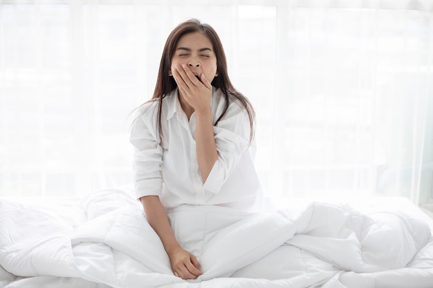 Aziatische vrouw het glimlachen vrouwenzitting op bed en het uitrekken zich in de ochtend bij slaapkamer na w