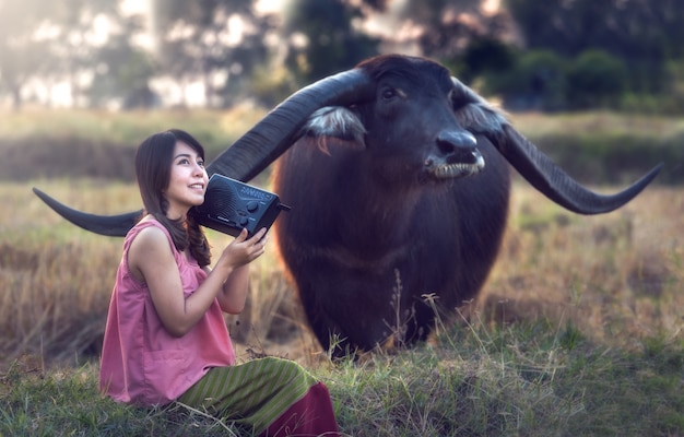 Aziatische vrouw het luisteren radio met haar buffels, Thailand