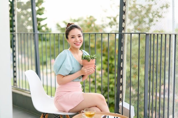 Aziatische vrouw houden en kijken naar plant ingemaakt op balkon in appartement in de ochtend