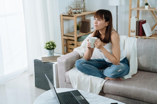 aziatische vrouw houdt een mok vast en neemt een pauze op een vakantieochtend. mooie dame kijkt uit het raam en geniet van haar thee en de verfrissende ochtend.