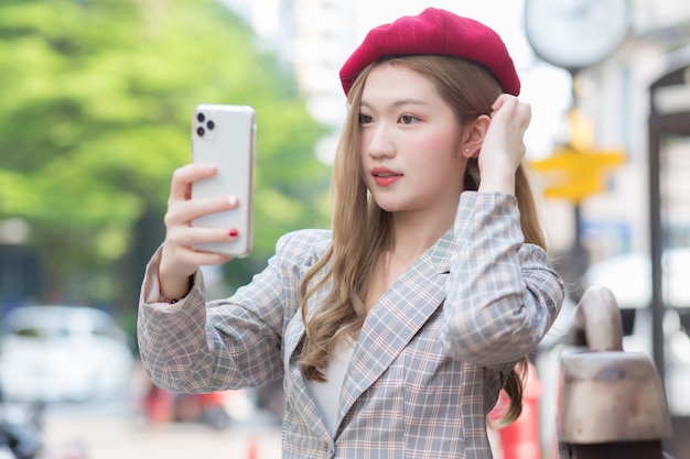 Aziatische vrouw in bronzen haar neemt selfie foto door smartphone op straat als achtergrond.