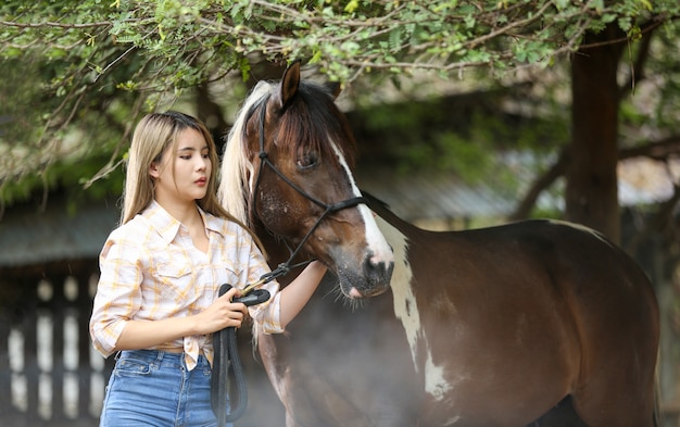 Aziatische vrouw in een cowgirl-kostuum staat met een paard op een veeboerderij.