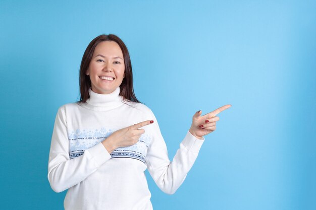 Aziatische vrouw in een Kerstmissweater wijst met haar wijsvingers op een lege ruimte voor tekst