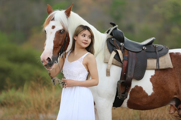 Aziatische vrouw in een lang jurkkostuum staat met een paard op een veeboerderij.