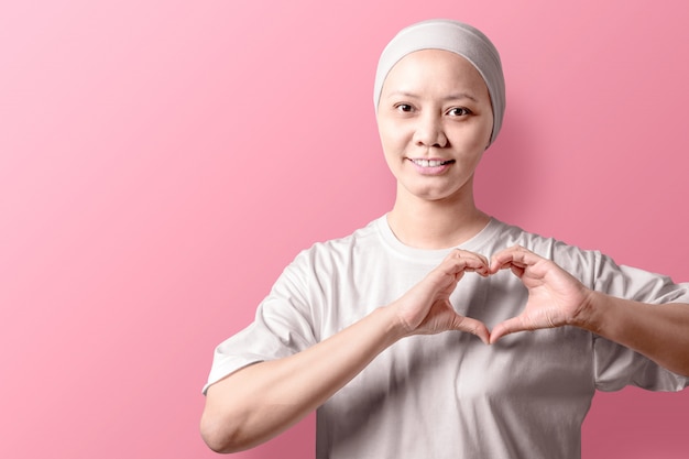 Aziatische vrouw in een wit overhemd die een hartteken met haar handen op roze tonen