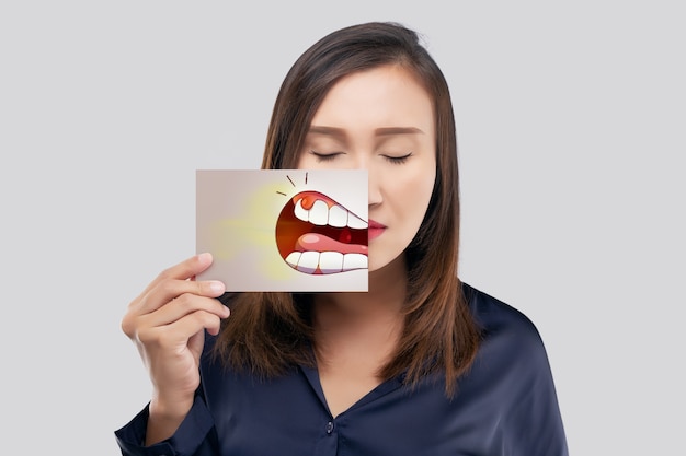 Aziatische vrouw in het donkerblauwe shirt met een papier met de parodontale en gingivitis cartoon afbeelding van zijn mond tegen de grijze achtergrond