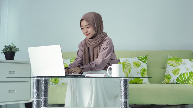 Aziatische vrouw in hijab die vanuit huis werkt met haar laptop