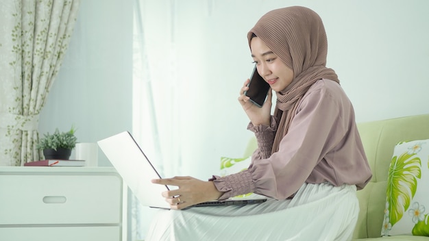 Aziatische vrouw in hijab online thuis bespreken via mobiel