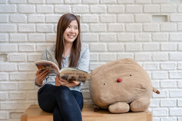 Aziatische vrouw in jeans pak zitten en het lezen van het tijdschrift in de woonkamer