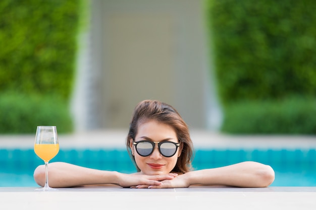 Aziatische vrouw in pool met glas jus d&#39;orange