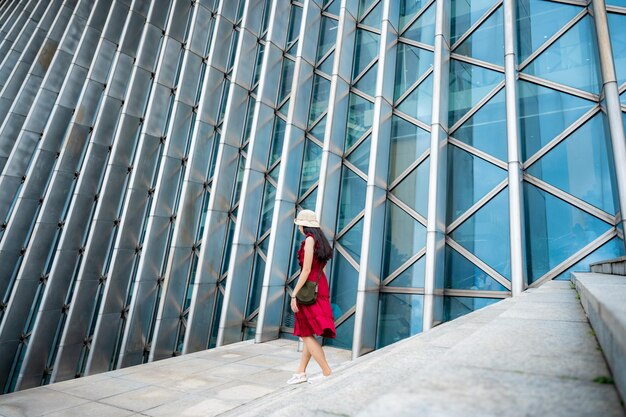 Aziatische vrouw in rode jurk bij modern gebouw vrouwelijk meisje met stedelijke stadslevensstijl