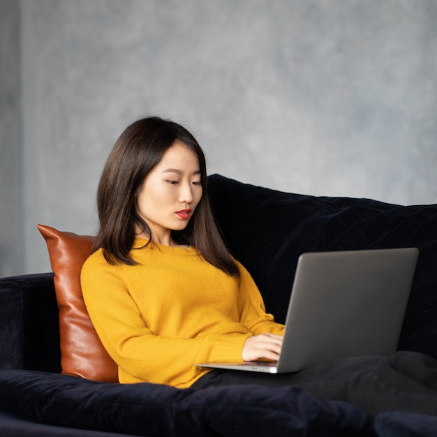 Aziatische vrouw kijken naar laptop, thuis werken, liying op de bank. ongelukkig, boos japanse vrouw