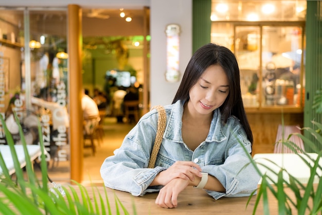 Aziatische vrouw kijkt naar het digitale horloge en zit in het café.