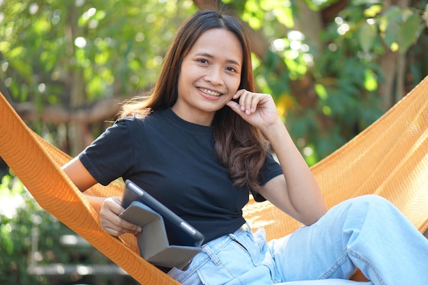 Aziatische vrouw kijkt naar verdiensten op een computer In een sinaasappelspread in een coffeeshop waar ze te midden van de groene natuur naar haar werk kan