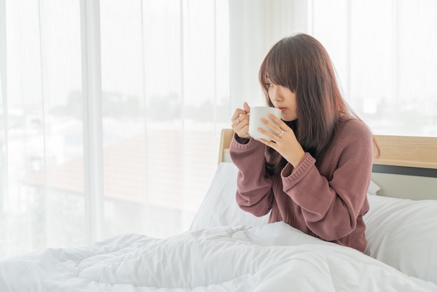 Aziatische vrouw koffie drinken op bed in de ochtend