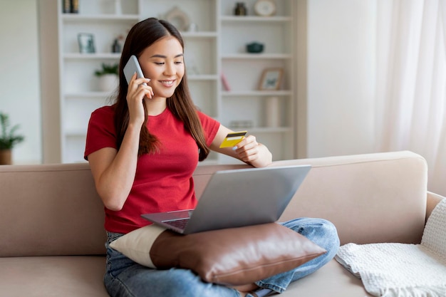 Aziatische vrouw maakt online aankopen via telefoon met laptop en creditcard