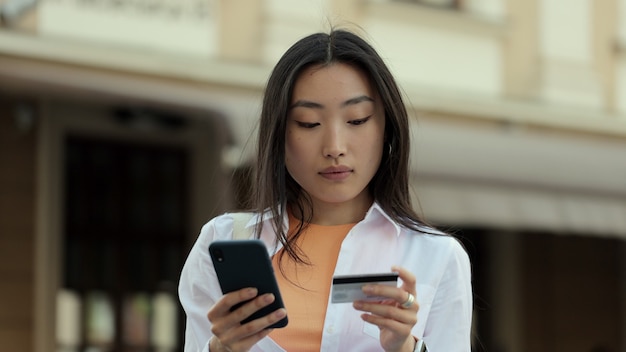 Aziatische vrouw maakt online betalingen via internet vanaf bankkaart op smartphone student meisje op straat met creditcard en telefoon vrouw viert een succesvolle aankoop