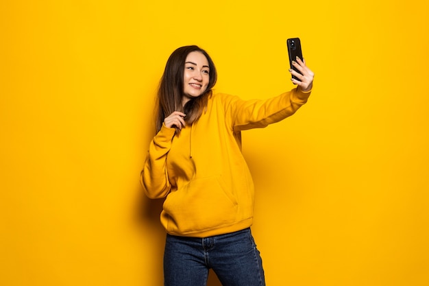 Aziatische vrouw maakt selfie foto op smartphone op gele muur