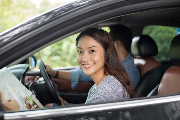 Aziatische vrouw met behulp van de smartphone en kaart en mannen auto rijden op road trip en gelukkig jong koppel met een