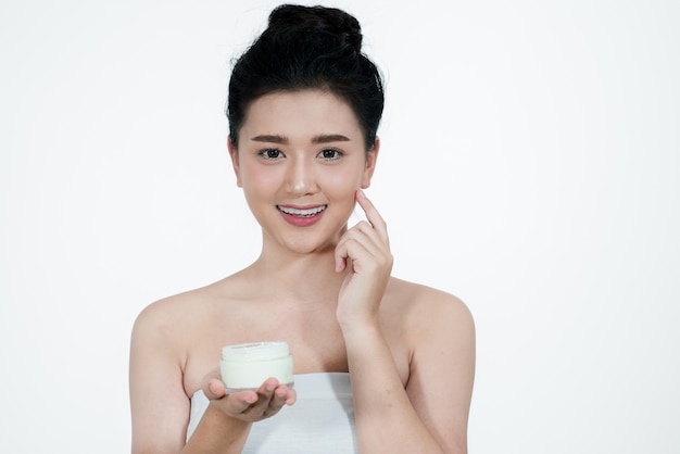 Aziatische vrouw met behulp van een huidverzorgingsproduct een witte achtergrond. meisje is blij met de huidcrème