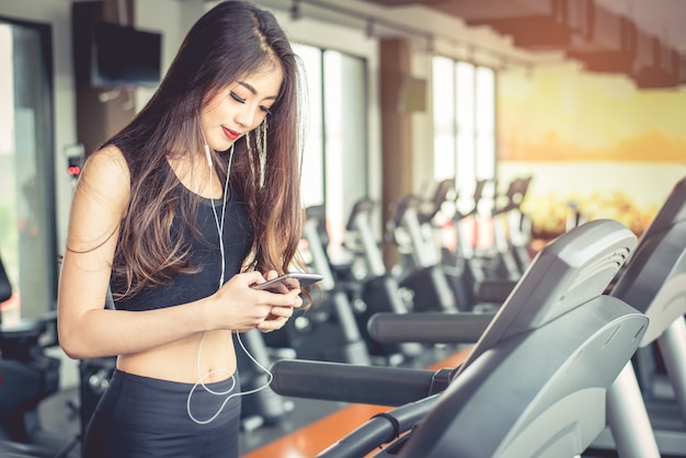 Aziatische vrouw met behulp van slimme telefoon bij het trainen of krachttraining bij fitness gym op de loopband
