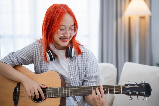 Aziatische vrouw met bril en koptelefoon die gitaar speelt terwijl ze op de bank in de woonkamer thuis zit Aziatische vrouwen die liedjes schrijven terwijl ze thuis gitaar spelen Compose song muziekconcept