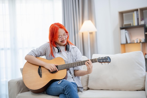 Aziatische vrouw met bril en koptelefoon die gitaar speelt terwijl ze op de bank in de woonkamer thuis zit Aziatische vrouwen die liedjes schrijven terwijl ze thuis gitaar spelen Compose song muziekconcept