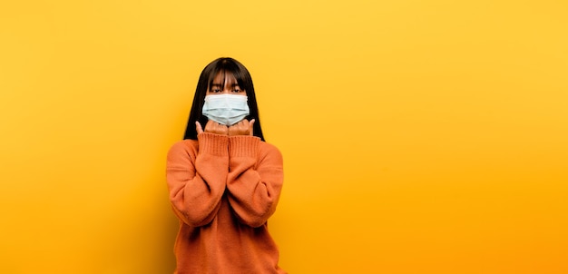 Aziatische vrouw met een masker Corona-viruspreventie rust in quarantaine Het sociale en emotionele afstandsconcept dat u overweegt te gaan. meisje met een medisch masker gele scène studiofotografie