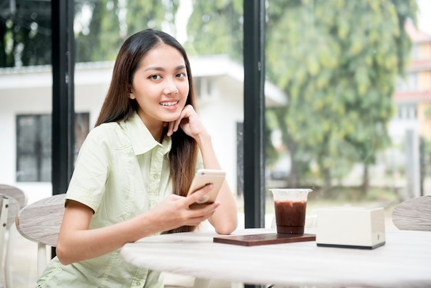 Aziatische vrouw met koffie op tafel met behulp van een mobiele telefoon in de coffeeshop