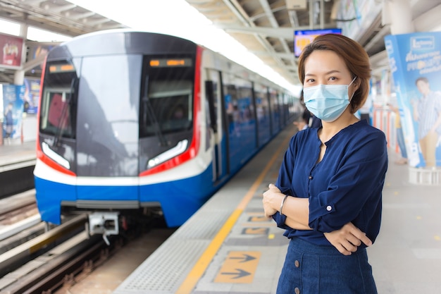 Aziatische vrouw met kort haar en een blauw shirt staat met haar arm over elkaar terwijl ze op de trein wacht op het station