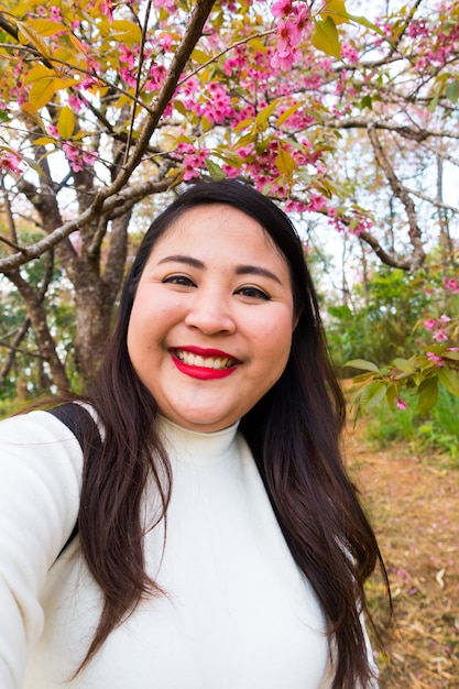 Aziatische vrouw met lang zwart haar neemt selfie lachend, portret met bloemen