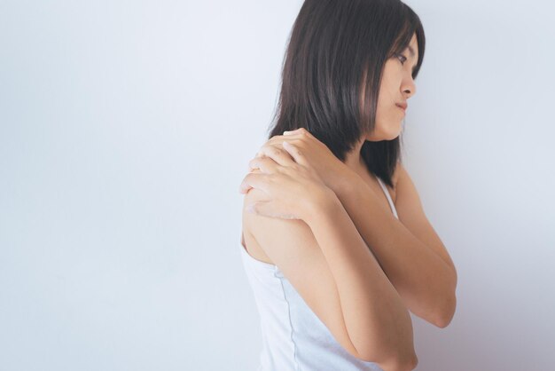 Aziatische vrouw met pijn in de schouderVrouwelijke hand die haar pijnlijk aanraakt