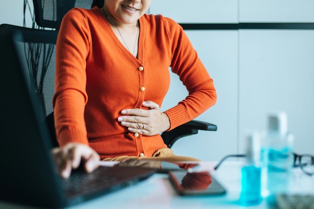 Aziatische vrouw met pijnlijke buikpijn tijdens het werken vanuit huis