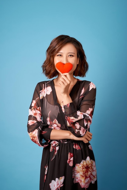 Aziatische vrouw met rood hart bedekt haar gezicht geïsoleerd op lichtblauwe achtergrond