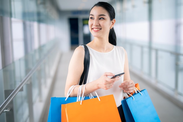 Aziatische vrouw met slimme telefoon met boodschappentassen loopt door de straten van de stad. Zomer stijl.