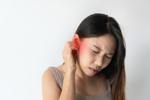 Aziatische vrouw met zere oor die lijden aan otitis met rood accent Benadrukt fronsend jong meisje van sterke oorpijn gevoel pijnlijk ongemak geïsoleerd op witte studio achtergrond Kopieer ruimte close-up