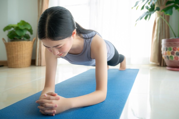 Aziatische vrouw oefent in haar woonkamer met een yogamat thuis