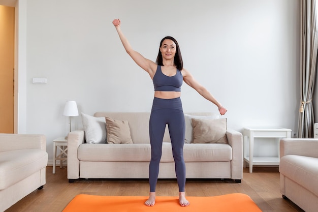 Aziatische vrouw oefent met dumbbells thuis Gelukkige vrouw doet armtraining met dumbbells