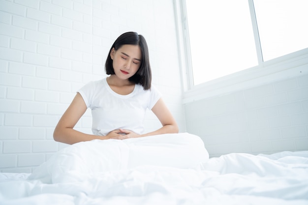 Foto aziatische vrouw ongelukkig liggend op het bed op zoek naar ziek, lijdt buikpijn in de slaapkamer