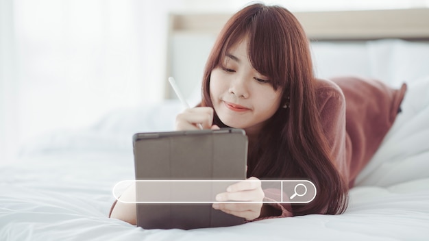 Aziatische vrouw op zoek naar informatie op een tablet op een wit bed Zoeken naar informatie dataconcept