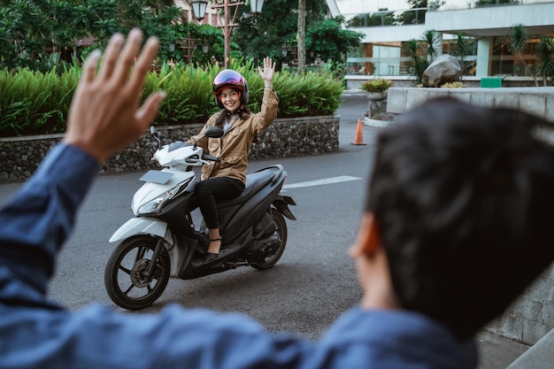 Aziatische vrouw rijdt op een motorfiets en zwaait met iemand langs de weg