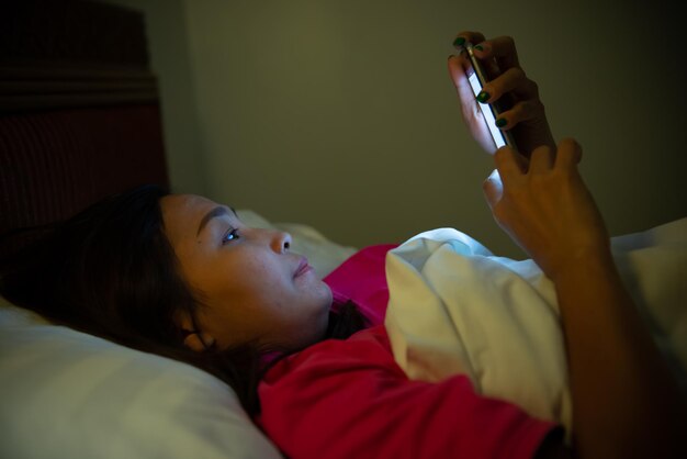 Aziatische vrouw speelspel op smartphone in het bed 's nachts Thailand peopleAddict social media