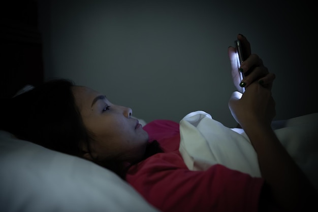 Aziatische vrouw speelspel op smartphone in het bed 's nachts Thailand peopleAddict social media