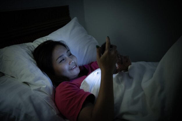 Aziatische vrouw speelspel op smartphone in het bed 's nachts Thailand peopleAddict social media