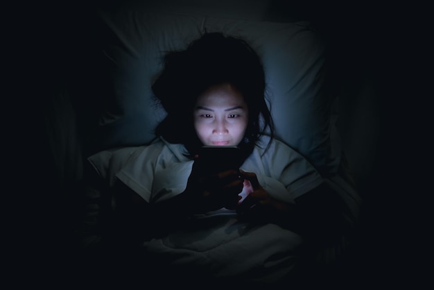 Aziatische vrouw speelspel op smartphone in het bed 's nachts Thailand peopleAddict social media